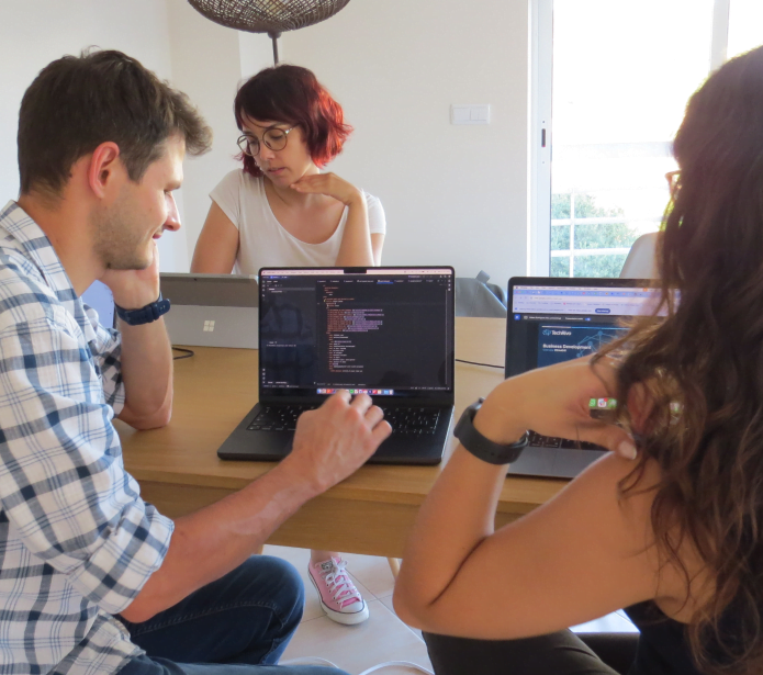 Founder of Praingol sitting down with two workers at a table, loking at a computer, discussing It consulting services